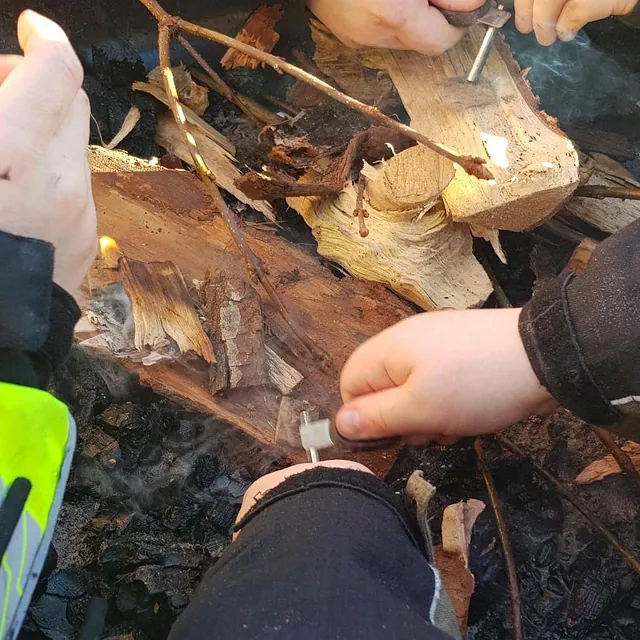 Barn tenner bål med tennstål på ved og kvister, iført varme ytterklær.